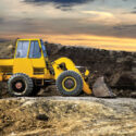 A bulldozer or loader moves the earth at the construction site against the sunset sky. Construction heavy equipment for earthworks