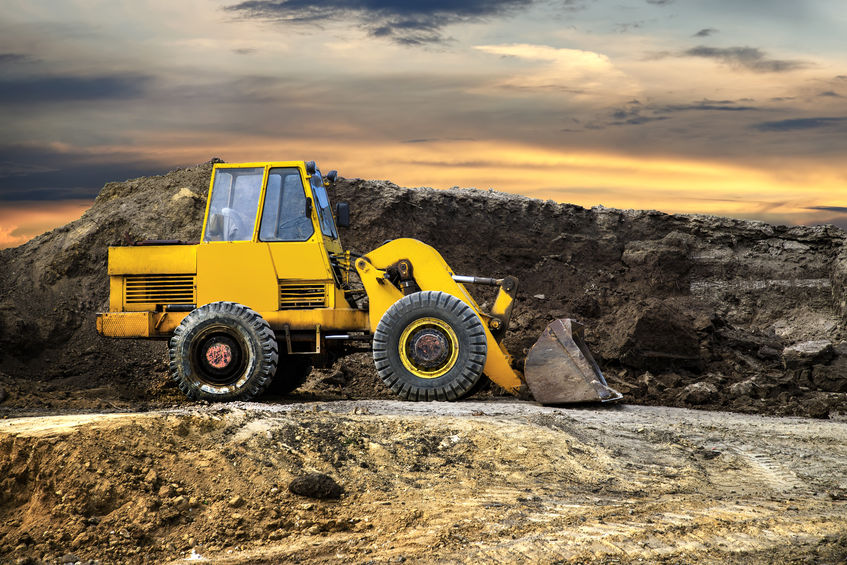 A bulldozer or loader moves the earth at the construction site against the sunset sky. Construction heavy equipment for earthworks